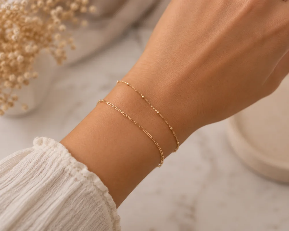 Two dainty gold permanent bracelets layered on a wrist